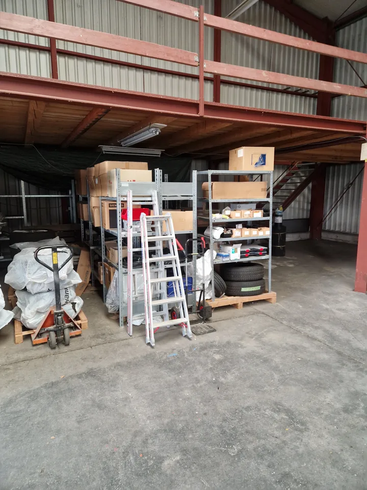 Werkstatthalle mit Paletten, Regalen und Leiter vor der Teilräumung